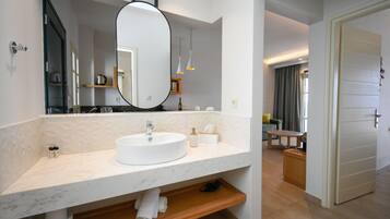 A modern bathroom with a large oval mirror, a white sink, and a wooden shelf.