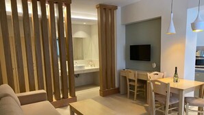 A modern living room with a sofa, a dining table with chairs, a TV mounted on the wall, and a wooden partition. - Elena Village (Kalymnos)