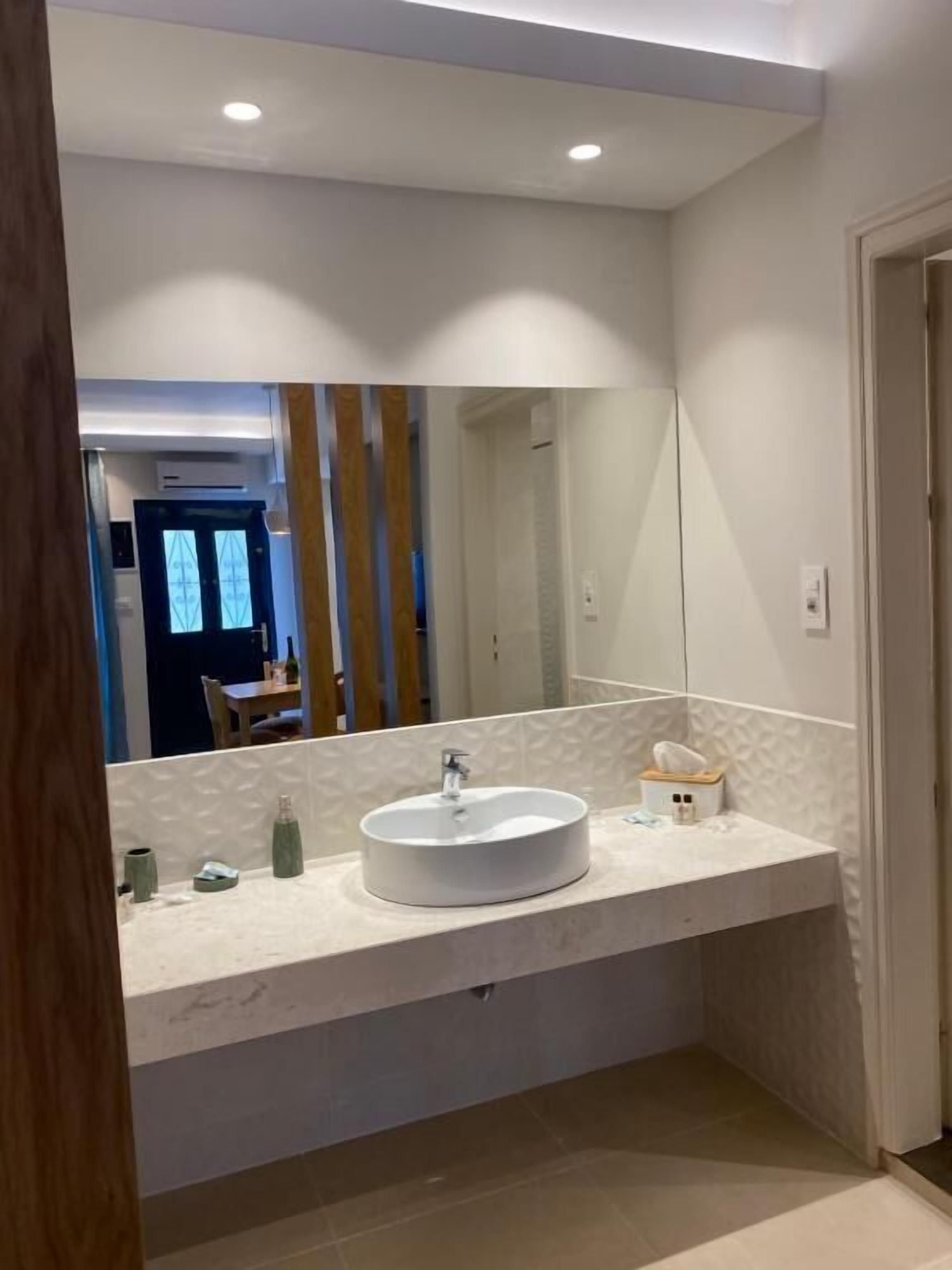 A modern bathroom with a large mirror, a round sink, and a towel dispenser.
