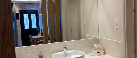 A modern bathroom with a large mirror, a round sink, and a towel dispenser.