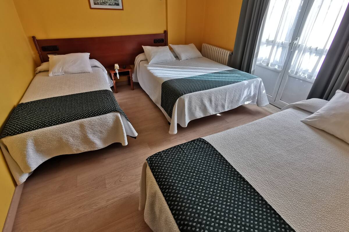 A hotel room with two beds, a wooden headboard, a small table with a lamp, and a painting on the wall.