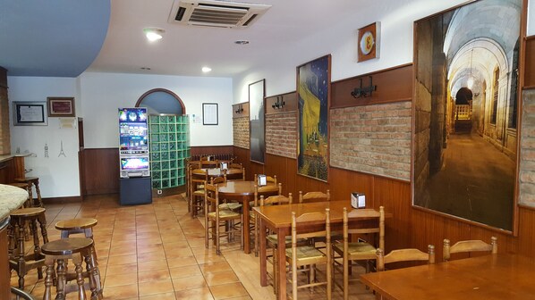 Um restaurante com mesas e cadeiras de madeira, um jukebox e um mural na parede.