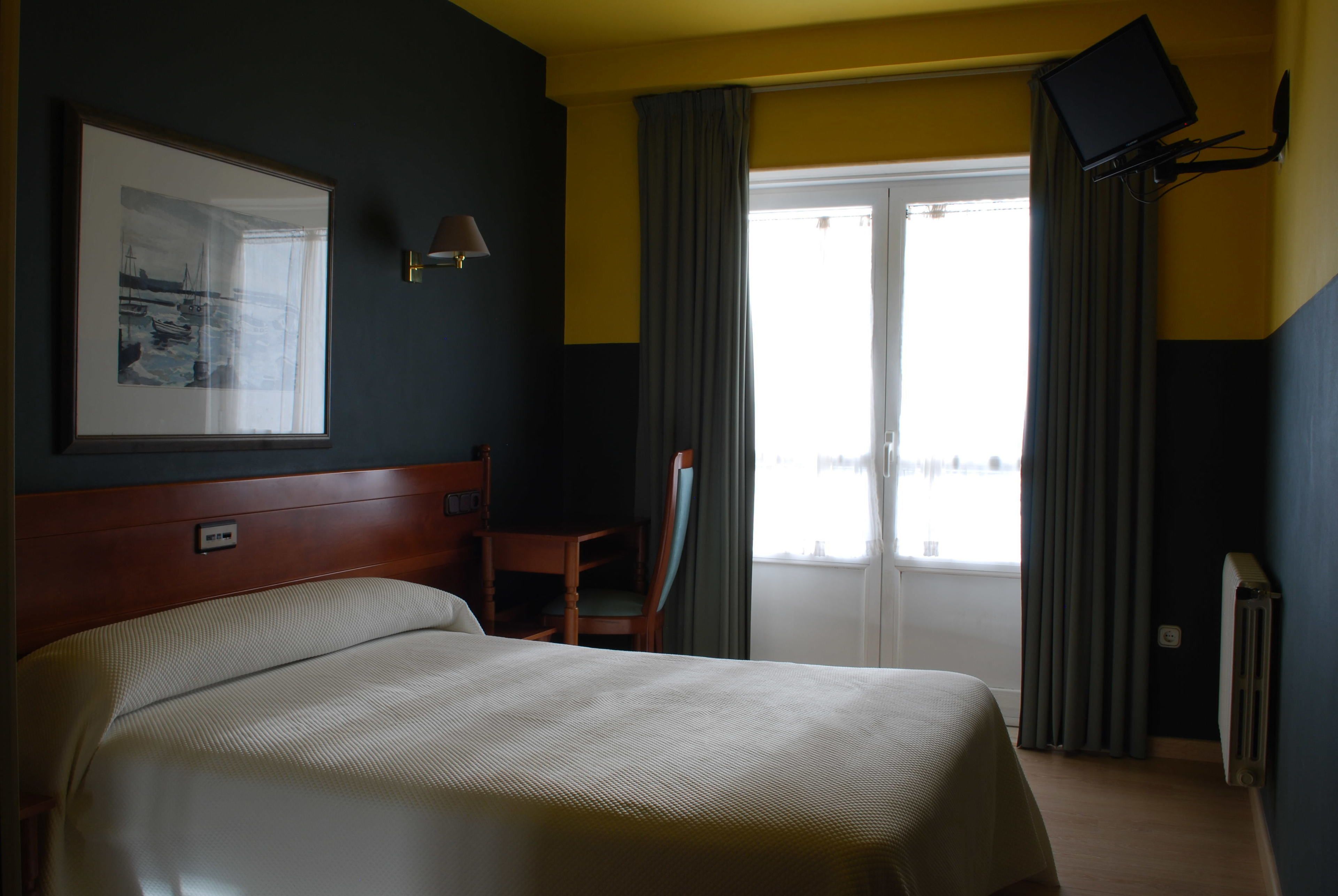 Une chambre d’hôtel équipée d’un lit, d’un bureau, d’une chaise, d’un téléviseur à écran plat fixé au mur et d’une fenêtre avec des rideaux.