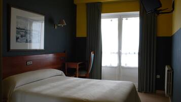 Une chambre d’hôtel équipée d’un lit, d’un bureau, d’une chaise, d’un téléviseur à écran plat fixé au mur et d’une fenêtre avec des rideaux.