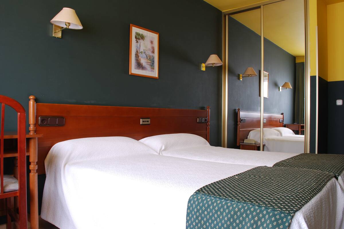 A hotel room with a wooden bed, a nightstand, a mirror, and two wall-mounted lamps.