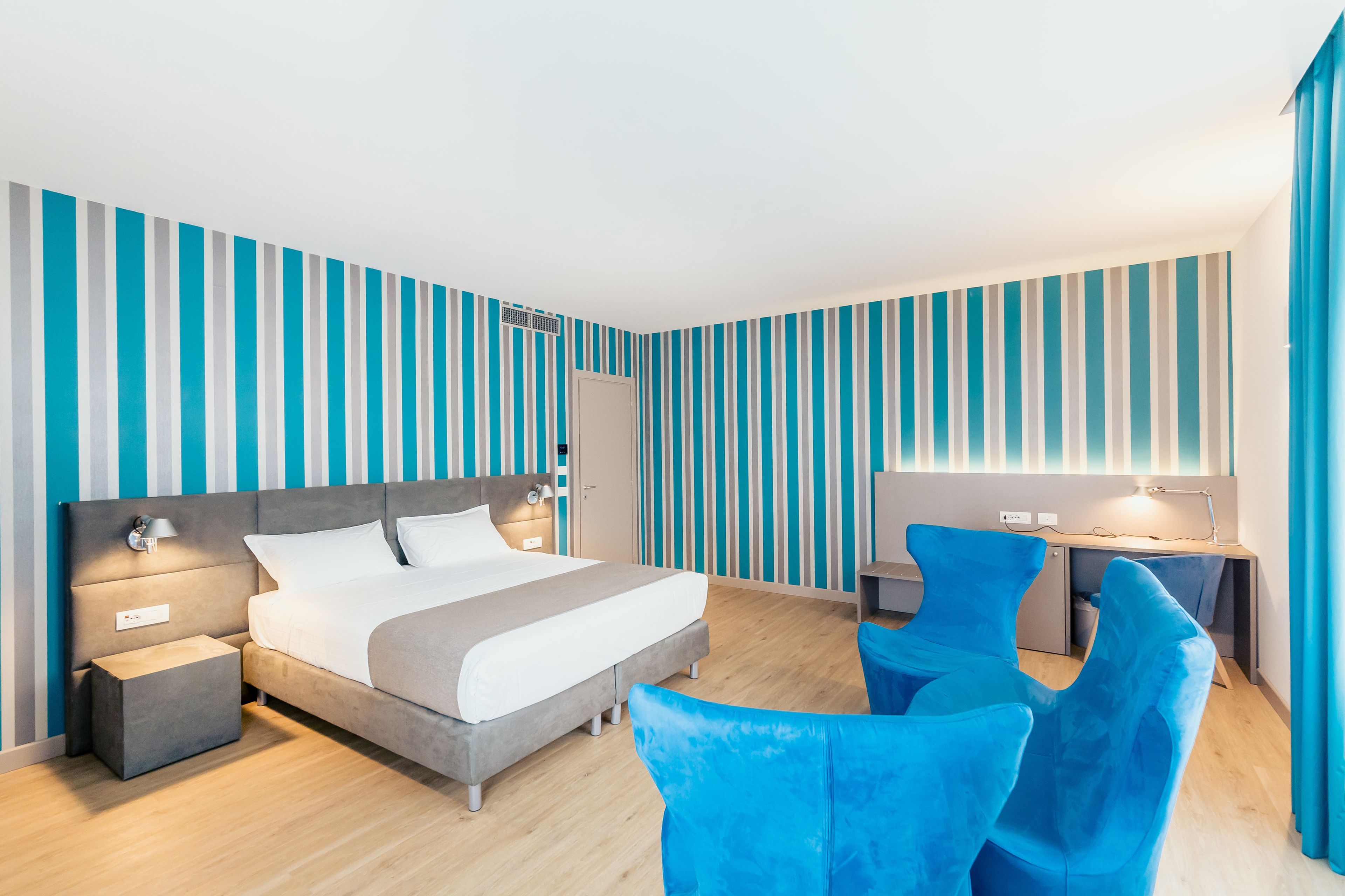 Una habitación de hotel moderna con una cama grande, un escritorio y dos sillas azules.