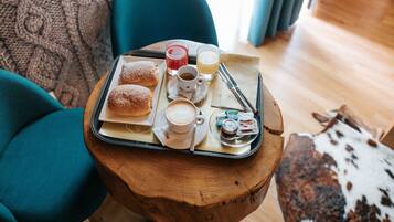A tray with pastries, coffee, and juice on a wooden table in a cozy room with teal chairs and a cowhide rug.