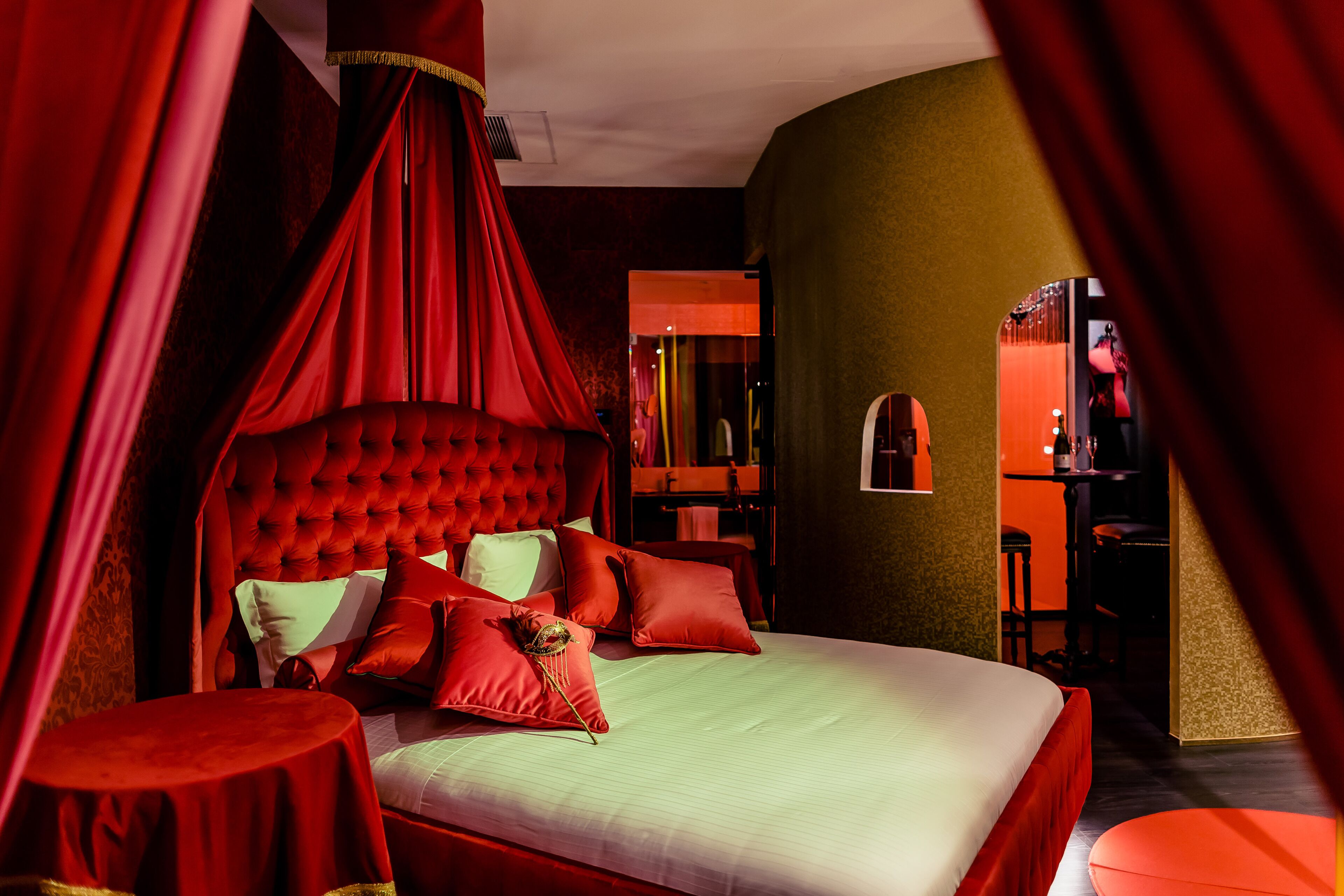 Een slaapkamer met een rode hemelbed, een ronde tafel en een spiegel.