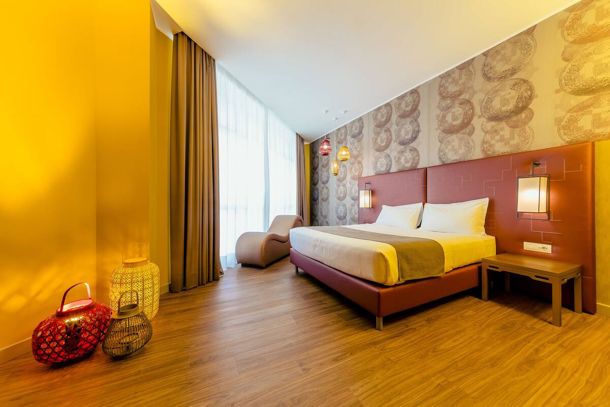 A modern hotel room with a large bed, a bedside table, a chair, and two decorative lanterns.