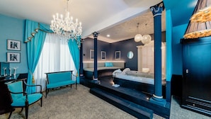 A modern hotel room with a large bed, a sitting area with a sofa and chairs, a chandelier, and a view of the city. - Diamante Mhotel (Collegno)