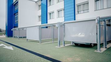 Un'area di parcheggio con una stazione di autolavaggio coperta, un edificio dalle pareti esterne blu e bianche e un vialetto pavimentato con indicazioni.