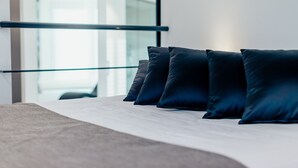 A bed with dark pillows and a white mattress, a glass railing, and a modern interior. - Diamante Mhotel (Collegno)