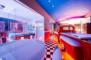 Um interior moderno com piso xadrez, um carro vintage vermelho e um letreiro 'Drive In'.