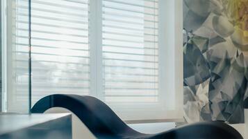 Ein modernes Zimmer mit einem schwarz gebogenen Sessel, einem Fenster mit Jalousien und einer Wand mit geometrischem Muster.