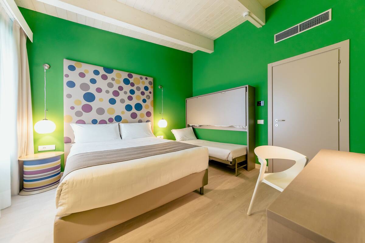 A room with a bed, bedside tables, a chair, a wardrobe, and a wall with a polka dot pattern.