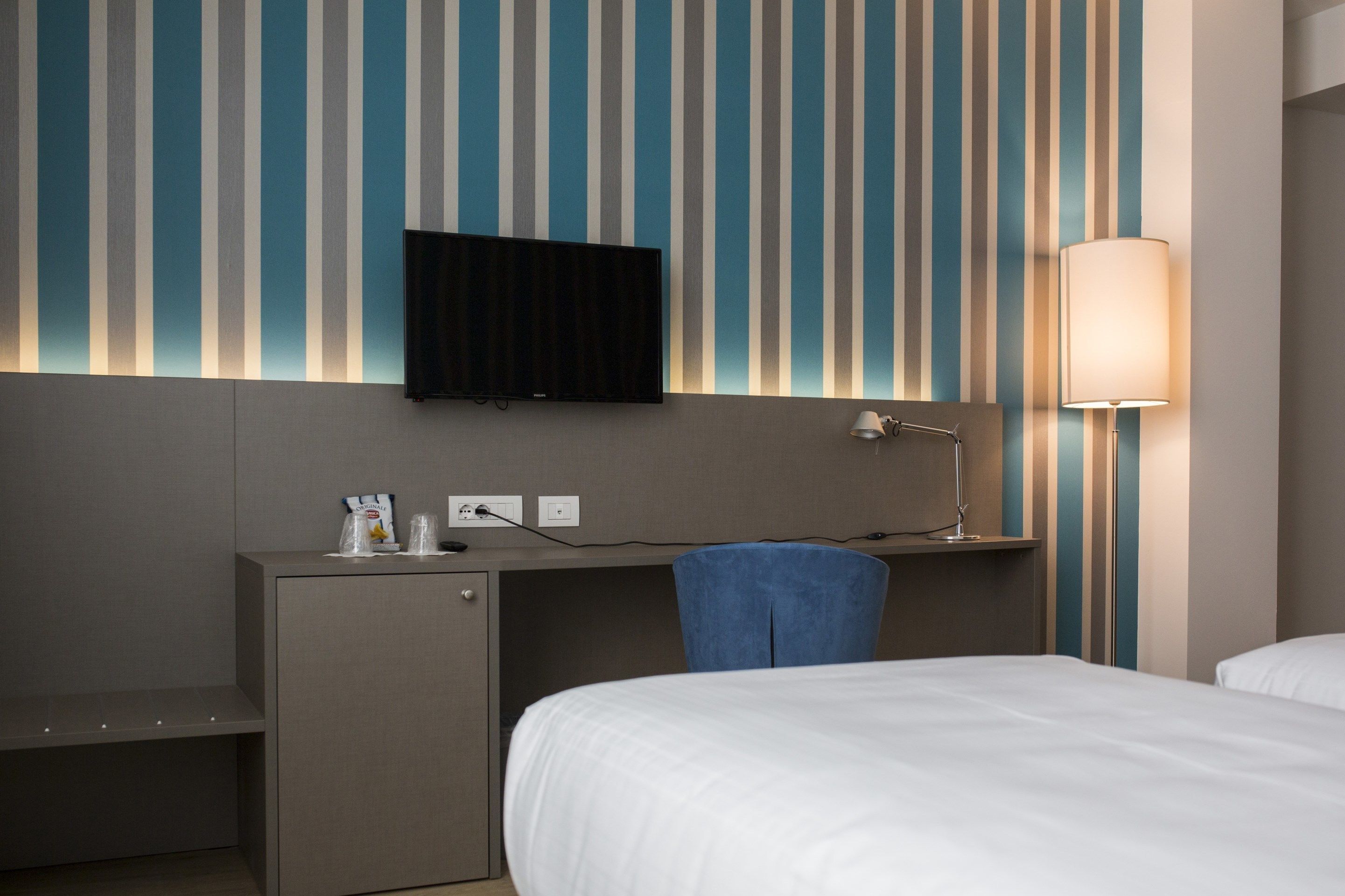 Une chambre d’hôtel comprenant un lit, un bureau avec une chaise, un téléviseur fixé au mur et une lampe.