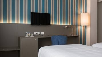 Une chambre d’hôtel comprenant un lit, un bureau avec une chaise, un téléviseur fixé au mur et une lampe.
