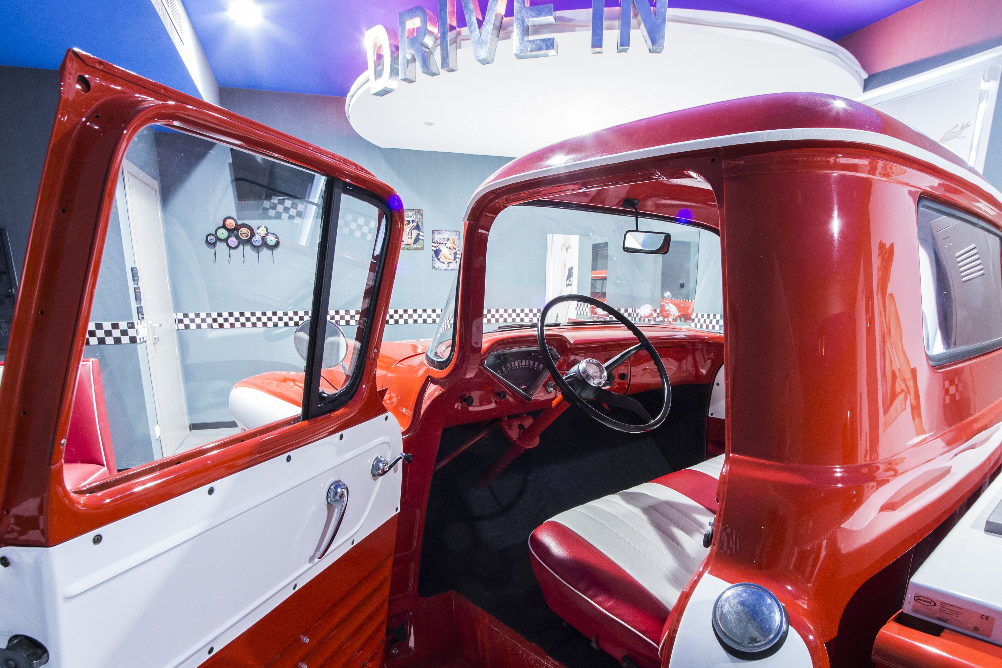 Un'auto d'epoca rossa e bianca con volante, cruscotto, luce interna e pavimento a scacchi.