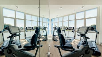 Un gimnasio con varias cintas de correr y bicicletas estáticas, ventanas amplias y suelo de madera.
