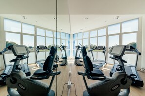 A gym with multiple treadmills and stationary bikes, large windows, and a wooden floor. - Diamante Mhotel (Collegno)