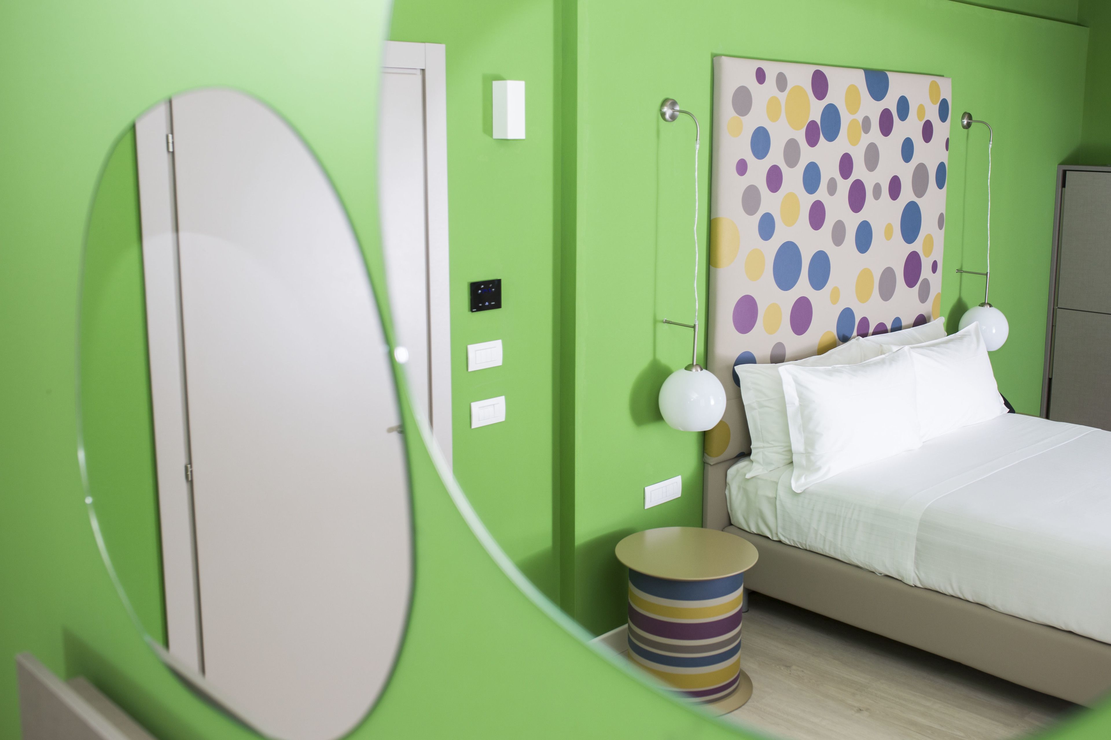 Una stanza con un letto, un comodino, uno specchio e una parete a pois.