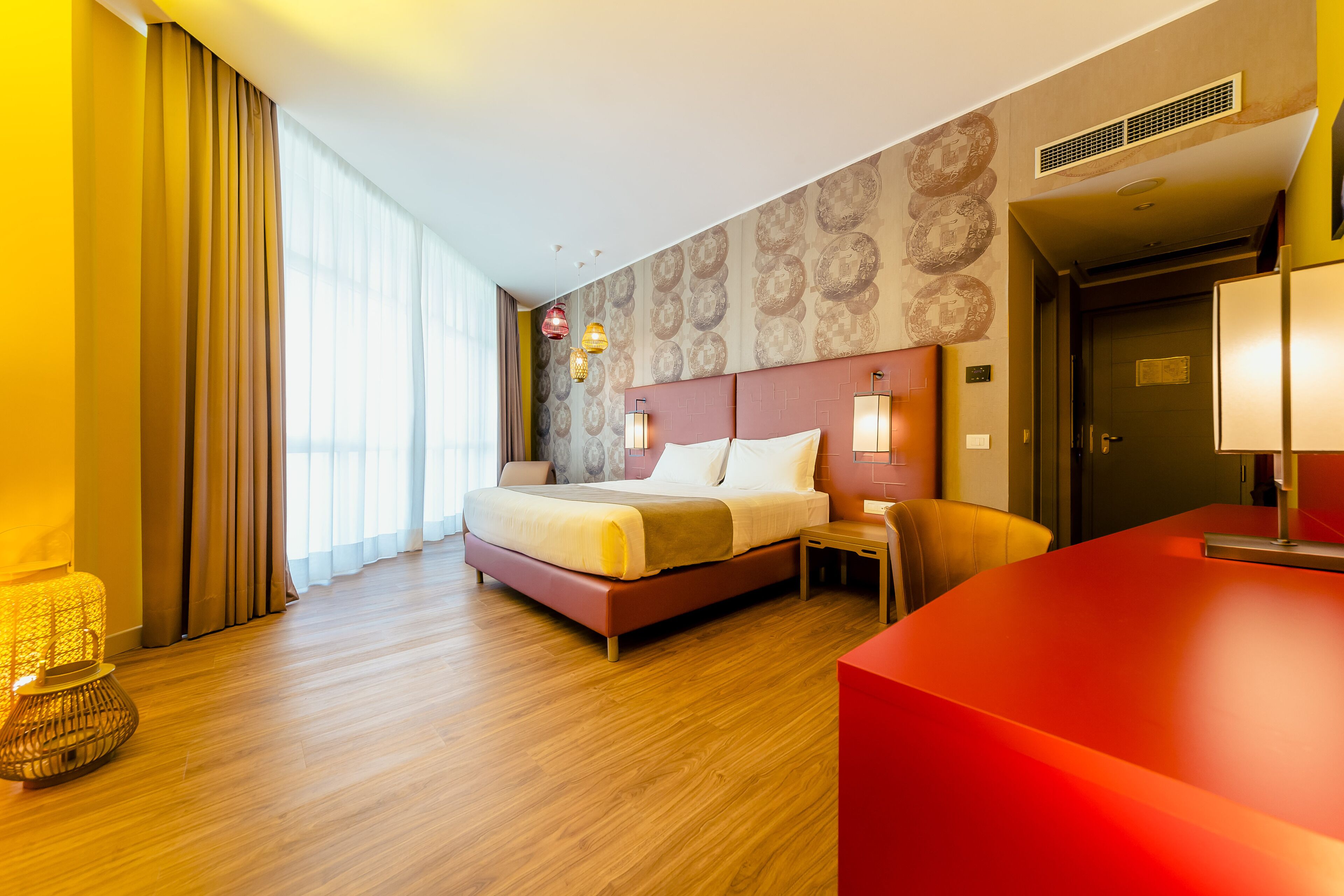 A modern hotel room with a large bed, a desk, and a red accent wall.