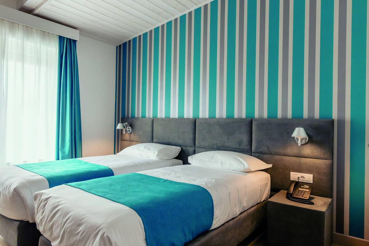 A hotel room with two beds, a nightstand with a phone, and a striped wall.