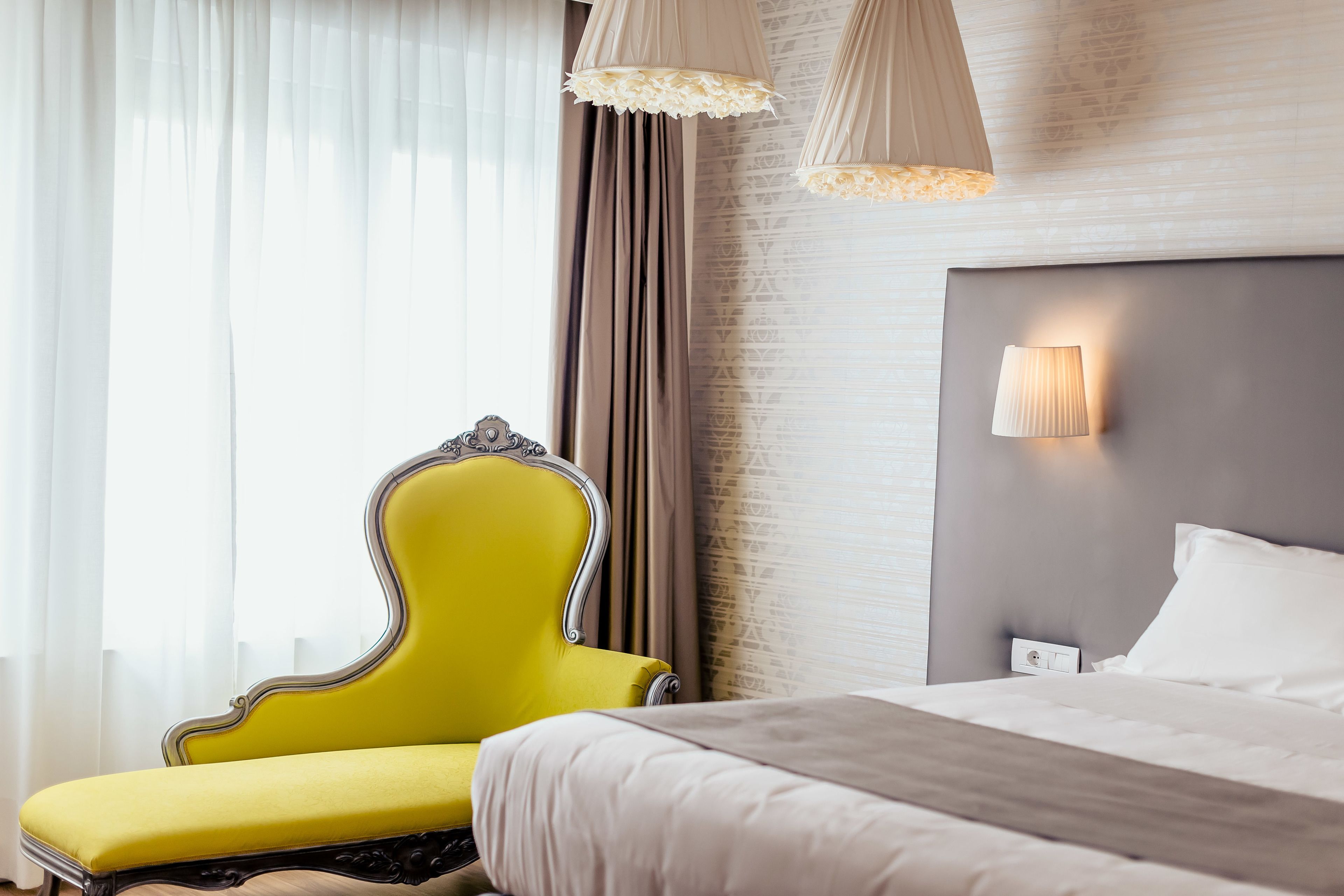 A hotel room with a bed, a yellow armchair, and a wall-mounted lamp.