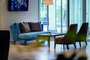 A modern living room with a blue sofa, a green coffee table, and two brown armchairs. - Diamante Mhotel (Collegno)