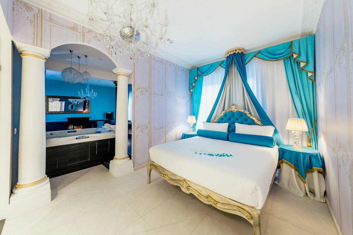 A luxurious bedroom with a large bed, a vanity with a mirror, and a chandelier.