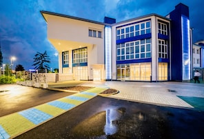 Um edifício moderno com telhado plano, amplas janelas e área de entrada pavimentada.