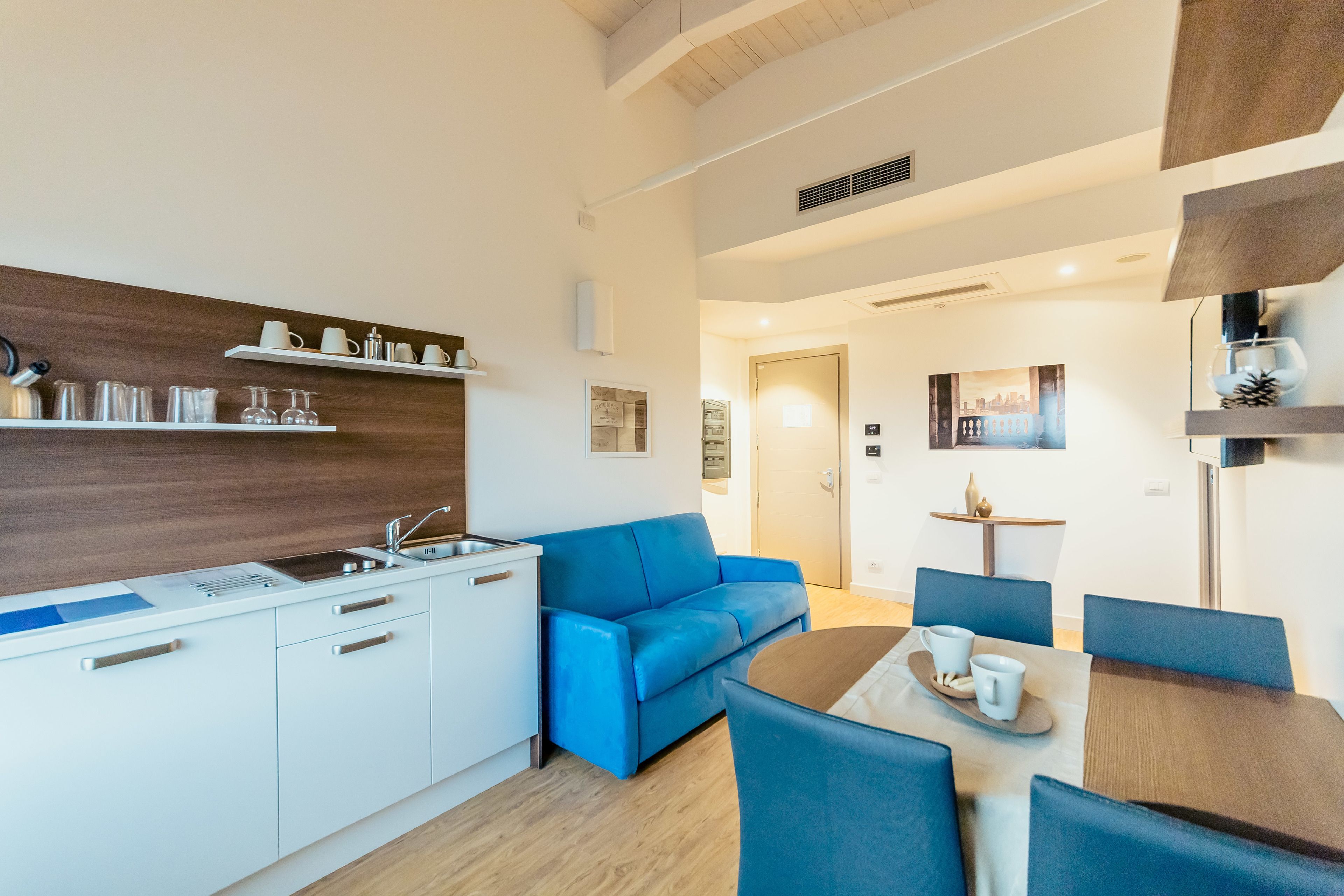 Una cocina moderna con armarios blancos, un sofá azul y una zona de comedor con una mesa y sillas.