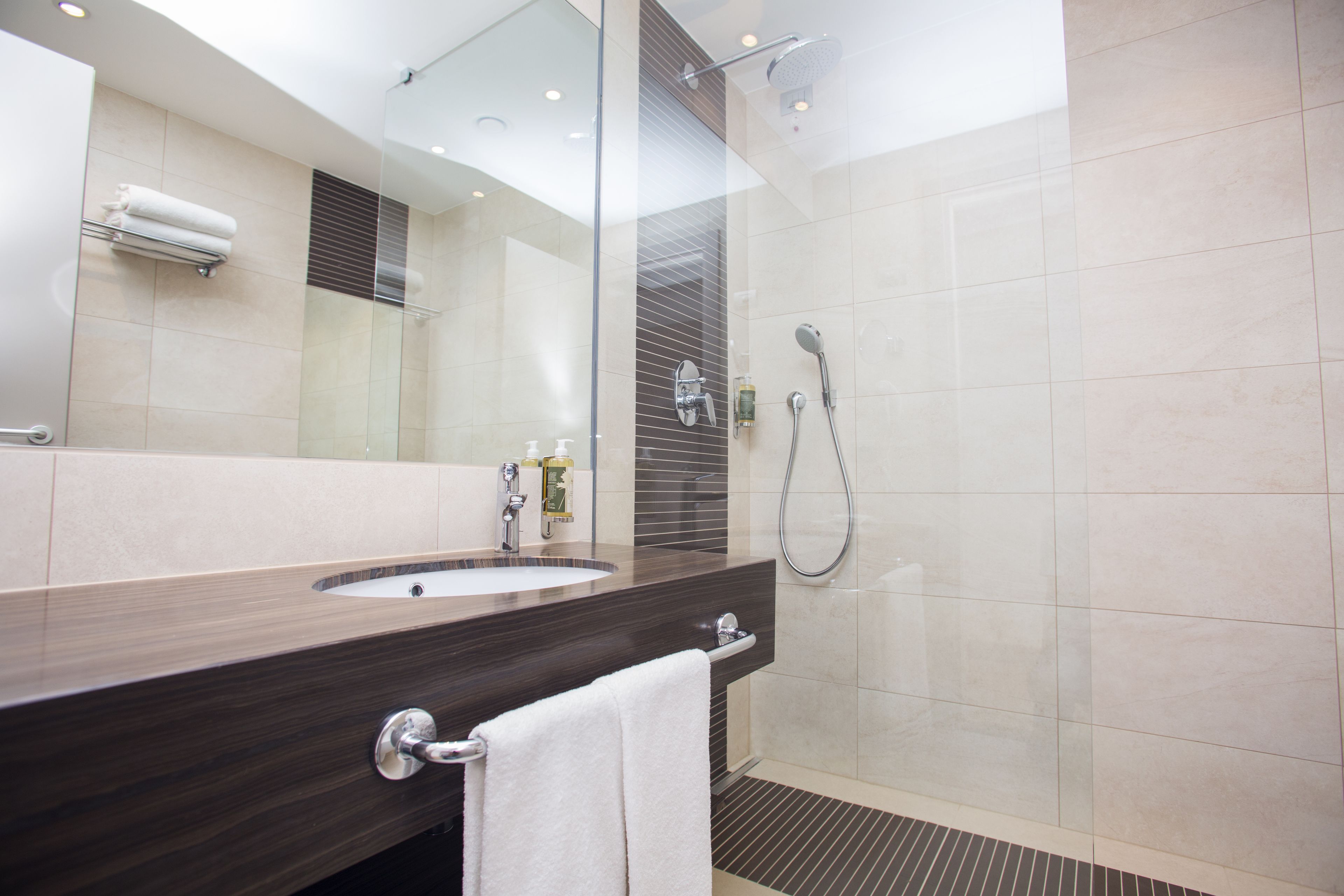 Une salle de bain moderne avec un meuble-lavabo en bois foncé, un grand miroir et une douche séparée par des parois en verre.