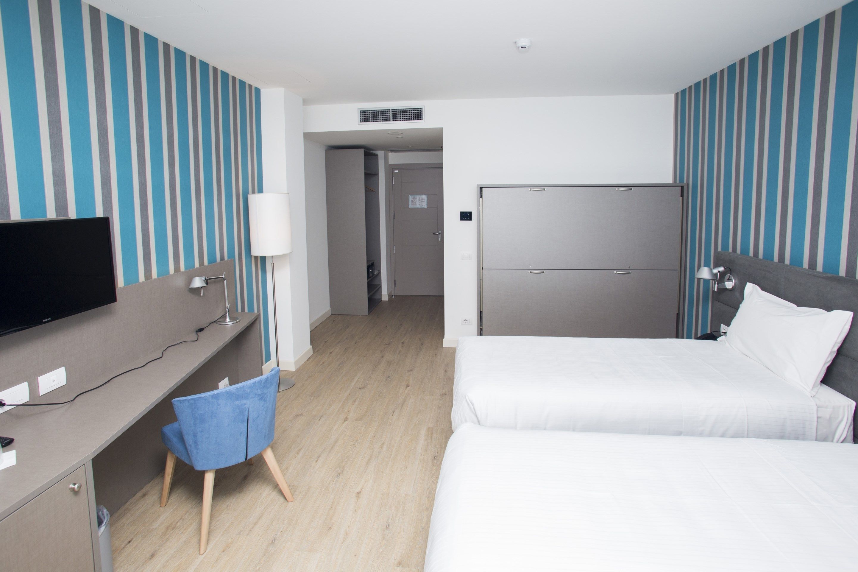 A hotel room with a bed, a desk, a chair, a TV, and a wardrobe.