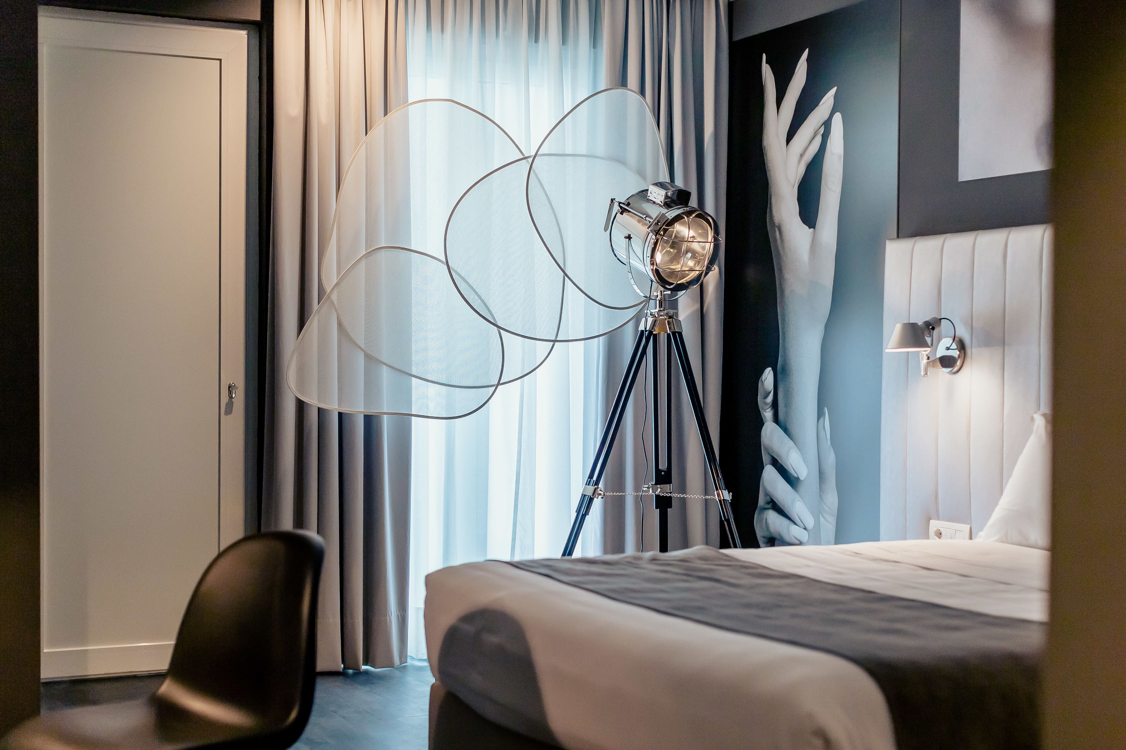 Una camera d'hotel con un letto, una sedia, una lampada da terra e una parete con un motivo a impronte di mano.