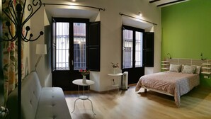 A bedroom with a bed, a sofa, a small table with a vase, and two windows with shutters. - El Granado Hostel (Granada)