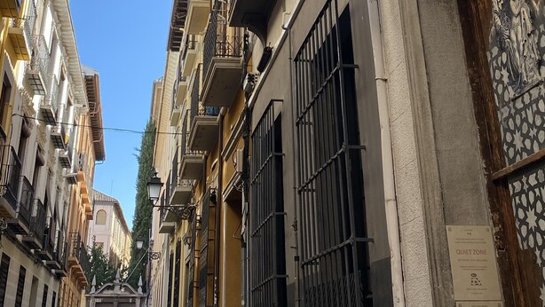 A narrow street with buildings featuring balconies and a sign with a geometric design. - El Granado Hostel (Granada)