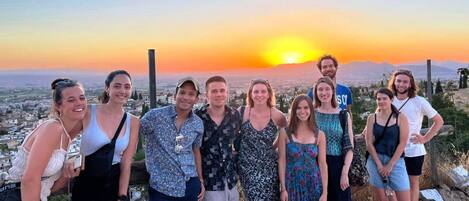 Un grupo de personas de pie en una colina, con un atardecer de fondo.