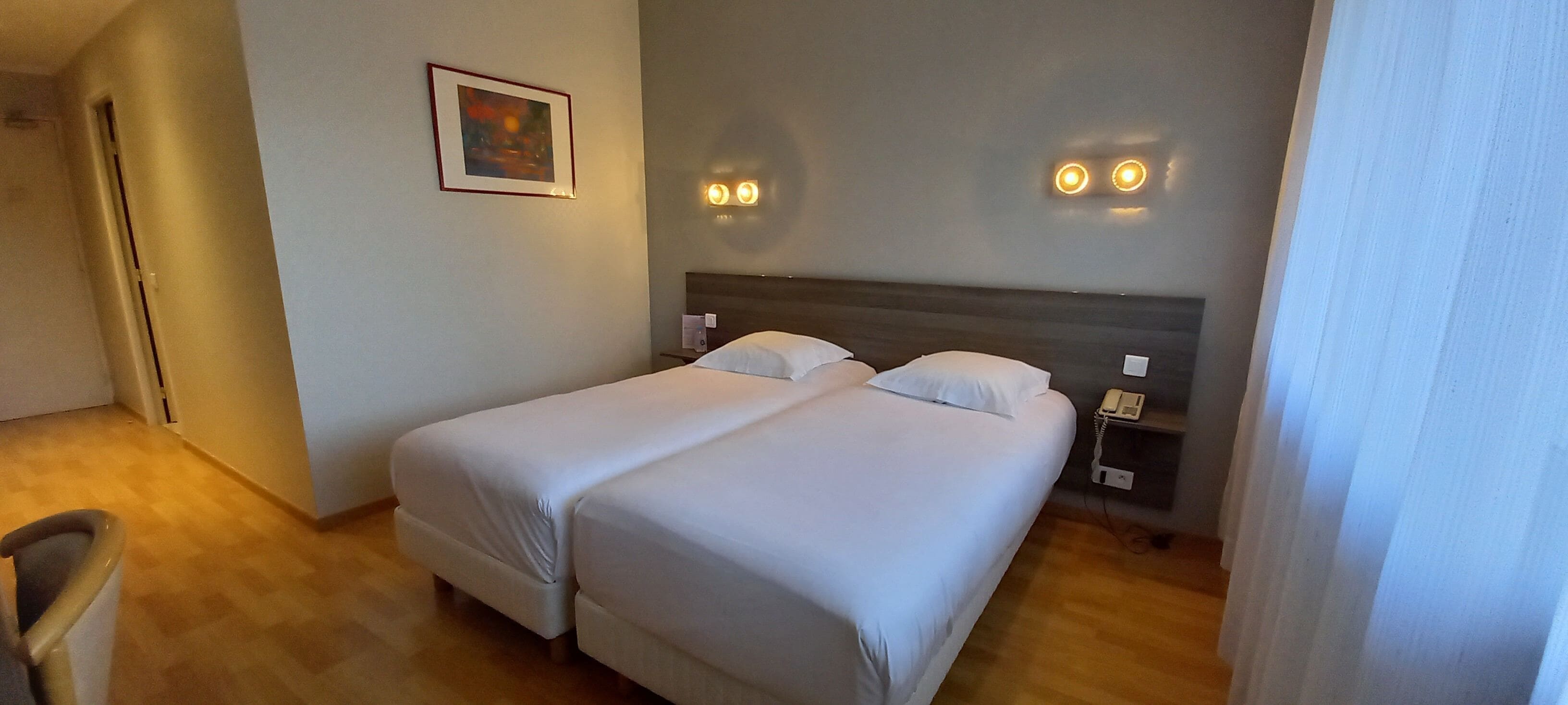 Een hotelkamer met twee bedden, een nachtkastje met een telefoon en een schilderij aan de muur.