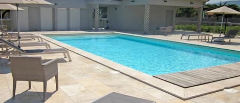 Una piscina con sillas de descanso y sombrillas, rodeada por un patio de baldosas.