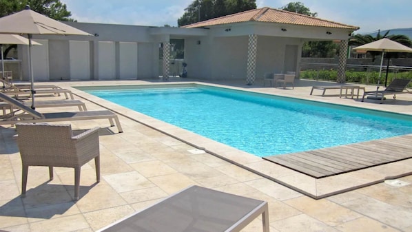 A swimming pool with lounge chairs and umbrellas, surrounded by a tiled deck.