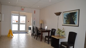 Un espace d’accueil comprenant un comptoir, des chaises, un ordinateur, une lampe, un tableau représentant un arbre et un panneau indiquant la sortie.