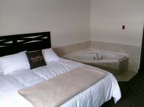 A hotel room with a bed, a large bathtub, and a headboard. - Auberge MacDonald Guest Inn (Iroquois Falls)