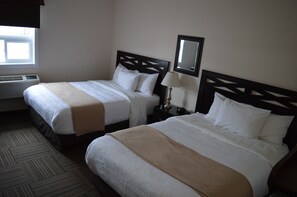A hotel room with two beds, a window, an air conditioning unit, and a nightstand with a lamp.