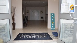 L’entrée d’un hôtel, avec un paillasson, une pancarte « Bienvenue » et un carillon.
