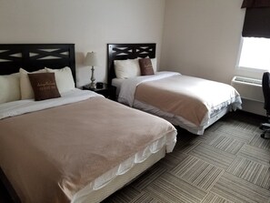 A hotel room with two beds, each with a headboard, a bedside table with a lamp, and a window with curtains.