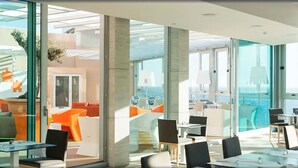 Un espace intérieur moderne avec des murs en verre, des meubles orange et blancs, et une vue sur l’océan.