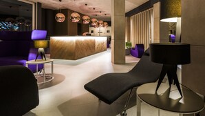Un hall d’entrée moderne avec un comptoir d’accueil, des sièges violets et des luminaires suspendus sphériques originaux.