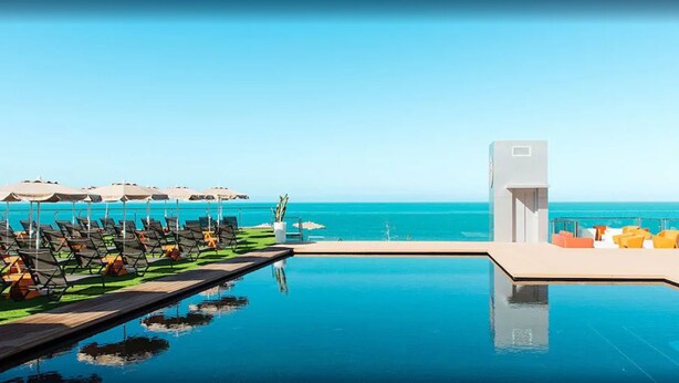 Un espace piscine doté de chaises longues et de parasols, avec vue sur une mer d’un bleu limpide.