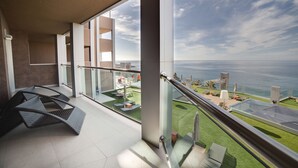 Un balcon moderne doté d’une balustrade en verre, offrant une vue sur un espace paysager aménagé et la mer.
